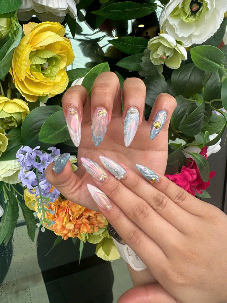 Long stiletto nails with 3D seashell charms, marble pastel art, and ocean-inspired nail designs showcasing intricate textures and fingernail artwork.