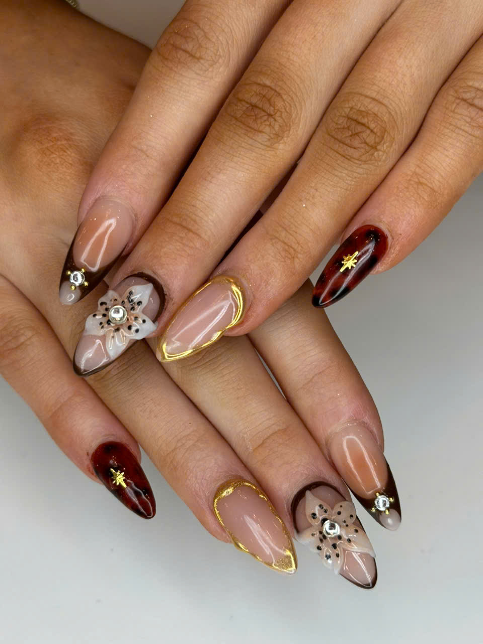 3D burgundy and gold nails with floral designs, featuring acrylic textures, gold edging, and dimensional bows for an elegant nail art look.
